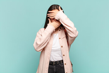 young pretty woman covering face with both hands saying no to the camera! refusing pictures or...