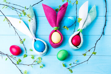 Easter eggs and the shape of rabbit ears and tree branches with green leaves, on a blue wooden background, selective focus, tinted image