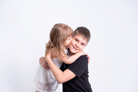 cute little sister kissing hugging her handsome older brother teenager on white background