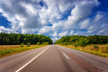 Empty summer highway in a hilly area, on the background of blue sky and white clouds