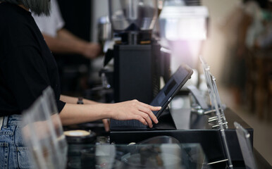 Side view of a young woman touching on the digital tablet to recive order from customer in coffee shop.