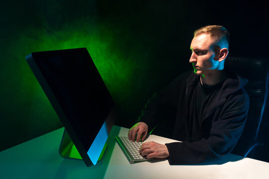 Programming. A man writes a computer program. A man at a computer on a black background with green lighting. The creation of computer applications.