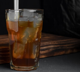 Coffee with ice cubes in a tall glass with tubes on a black background. Copy space