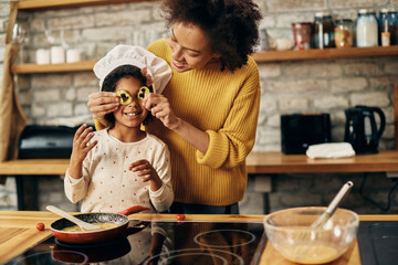 Playful black mother and daughter having fun with food while preparing meal in the kitchen.