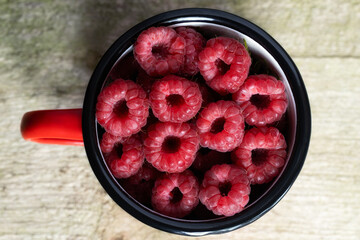  Raspberries in red mug on wooden table. Healthy eating and nutrition. Close up. Harvest Concept.