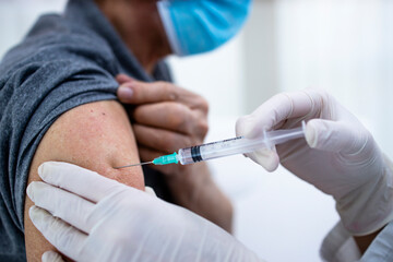 Close up view of an old man getting vaccine shot in his arm during corona virus pandemic.