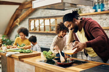 Happy African American father and daughter making scrambled eggs for breakfast in the kitchen.