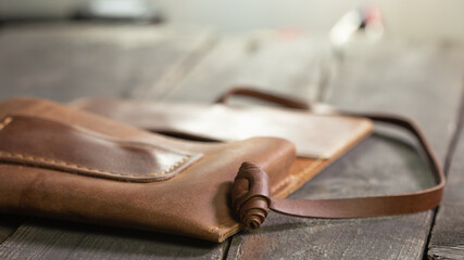 Brown style tobacco pouch leather on wood background. Craft product handmade. Hand sewing.