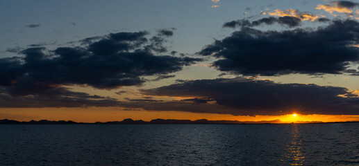 Obraz premium scenic and colorful sunset over the ocean with shimmering light on the waves and silhouette of mountains on the shore behind