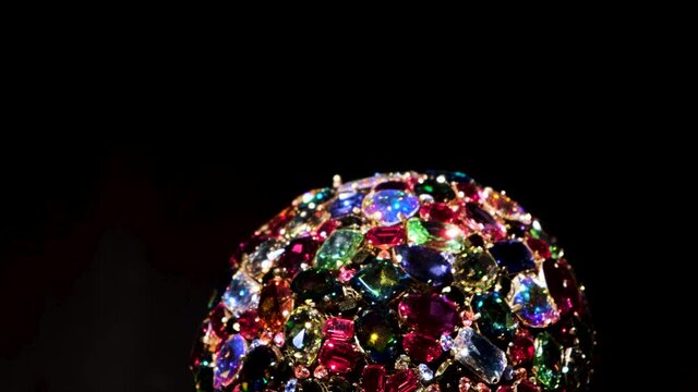 Close up of amazing luxury brooch with many colorful shiny gems. Concept. Rotating jewelry shining under spotlights isolated on black background. 