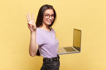 young pretty woman smiling and looking friendly, showing number three or third with hand forward,...