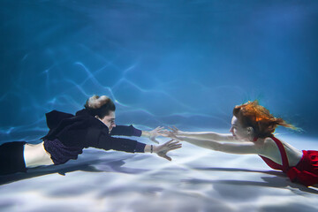 European guy and girl posing underwater in the pool. Young couple swims in the pool on a blue background