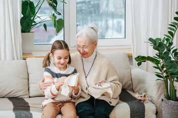 Grandmother teaches her granddaughter to embroider, they sit on the sofa at home © zzzdim