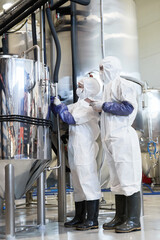 Vertical side view portrait of two workers wearing protective suits while using machines at modern...