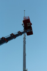 Obraz premium Maintenance of a communication tower, a lift at a height against a blue sky.