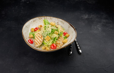 Delicious caesar salad with croutons, grilled chicken breast, grated parmesan cheese and cos lettuce, with sauce on black rustic background