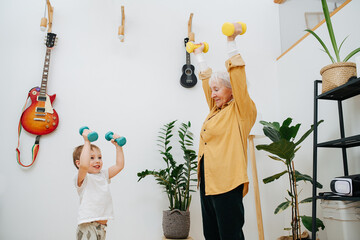 Senior woman and young grandson together do exercises by lifting dumbbells up