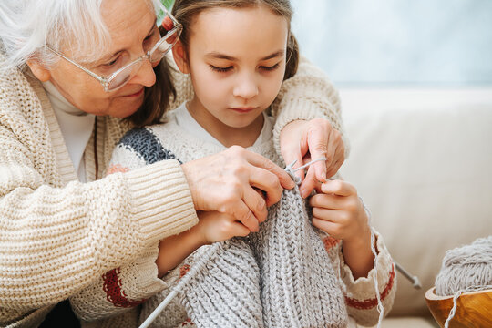 Senior woman teaches little girl how to knit wool threads with spokes