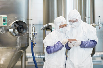 Waist up portrait of two workers wearing protective suits while using digital tablet at chemical factory, copy space