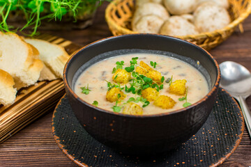 A bowl of homemade mushroom puree soup with herbs and bread on a wooden table. Homemade vegetarian mushroom soup with vegetables and bread.