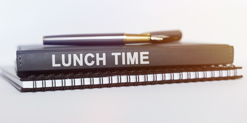 On the table are a notebook, a pen and a book. The book says - LUNCH TIME