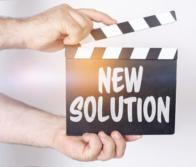 Obraz premium On a white background, a man holds a clapperboard in his hands on which it is written - NEW SOLUTION