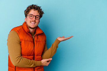 Young caucasian man wearing eyeglasses isolated on blue background showing a copy space on a palm...