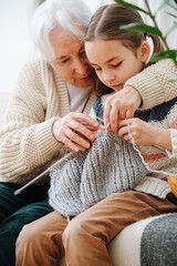 Elderly woman teaches little girl how to knit wool threads with spokes