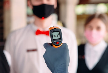 The Manager of a restaurant or hotel checks the body temperature of the staff with a thermal imaging device.