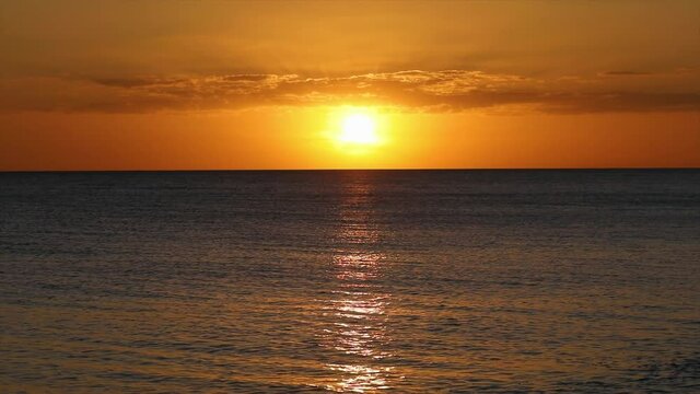 A cloudy glorious sunset over the Gulf of Mexico reflects upon the gentle waves of the sea as the sun nears the horizon.