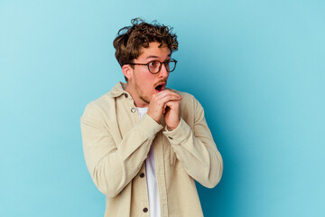 Young caucasian man wearing eyeglasses isolated on blue background praying for luck, amazed and opening mouth looking to front.