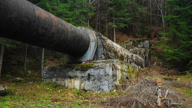 Old water supply adduction pipeline crossing through mountains and woodlands. The concrete pipe's support is full of moss. Latorita Mountains, Carpathia, Romania.