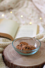 Bowl of chocolate chip cookies and open book on a bed. Selective focus. 