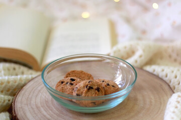 Bowl of chocolate chip cookies and open book on a bed. Selective focus. 