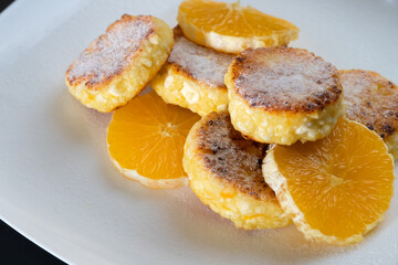 Cottage cheese pancakes with orange slices on a white plate sprinkled with powdered sugar. Beautiful, delicious breakfast