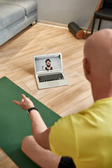 Sport and healthy lifestyle. Male fitness coach sitting on yoga mat at home, explaining workout...