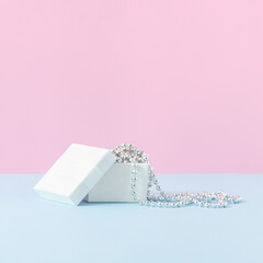 White gift box with pearl necklace on pastel blue table against pink wall. Creative minimal concept.