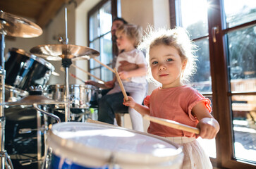 Portrait of small girl indoors at home, playing drums.