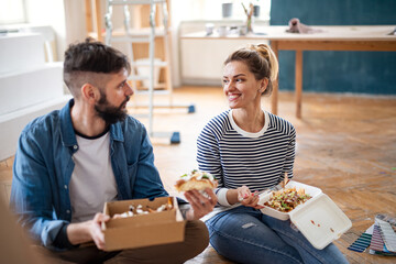 Couple eating lunch indoors at home, relocation, diy and food delivery concept.