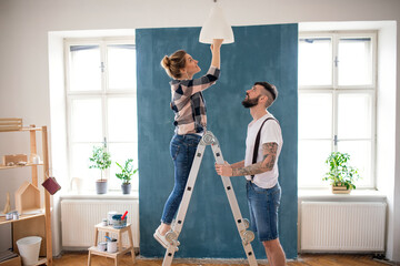 Mid adults couple changing light bulb indoors at home, relocation and diy concept. - obrazy, fototapety, plakaty