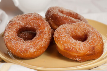 front view, medium distance, of three freshly baked sugar donuts, cooling on a round, yellow plate