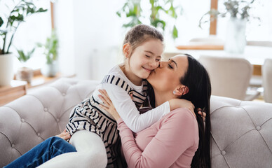 Obraz premium Mother with small daughter sitting on sofa indoors at home, kissing.
