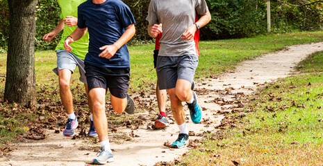 Four boys running together on a dirt path in a park