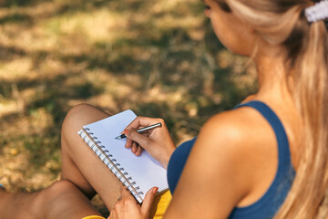beautiful young woman writing in her diary on the meadow