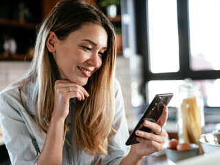 Beautiful woman drinking coffee and using the phone in the kitchen. Young woman enjoying in morning.