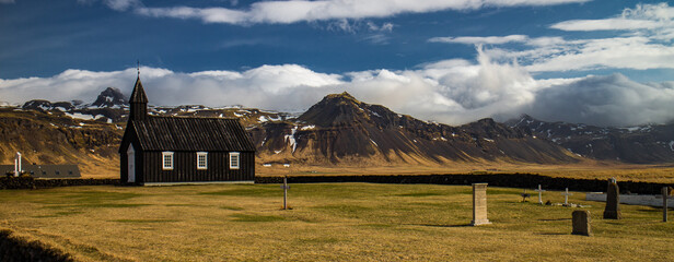 Budir church with cemetary and beautiful mountain landscape with blue sky in background in Iceland