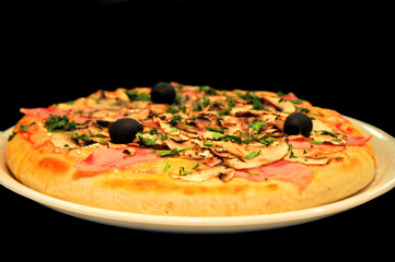 Delicious homemade pizza with mushrooms, ham, and olives on a white plate