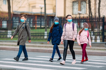 School children cross the road in medical masks. Children go to school.