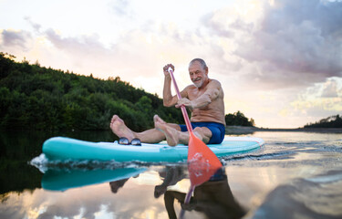 Senior man paddleboarding on lake in summer. Copy space.