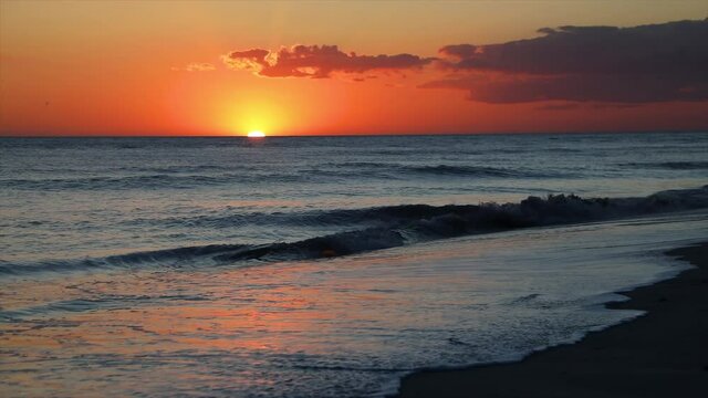 A beautiful seaside sunset over the Gulf of Mexico is viewed from a sandy beach with breaking waves at Sanibel Island, Florida.